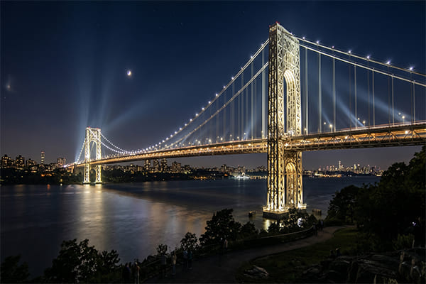 A large landmark bridge lit with powerful floodlights from a distance